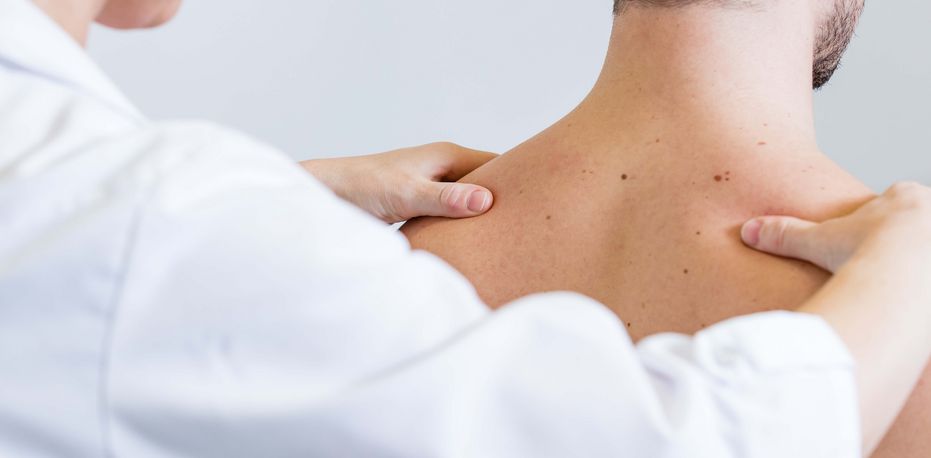 Ärztin untersucht Schultern eines Patienten
