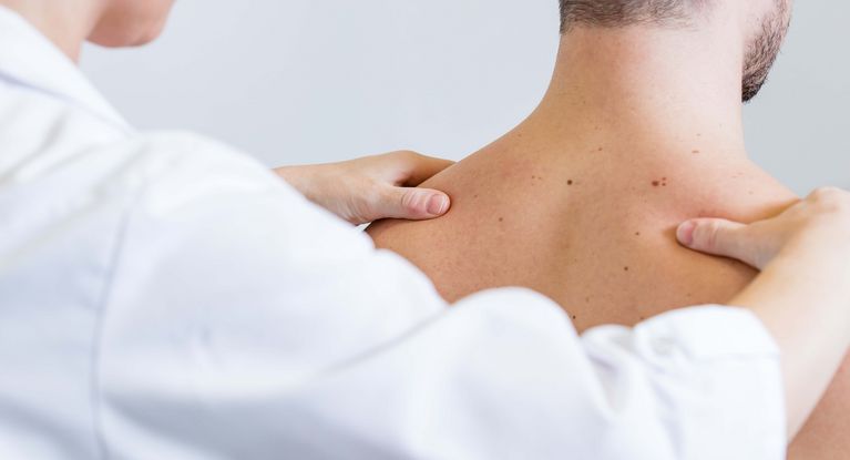 Ärztin untersucht Schultern eines Patienten