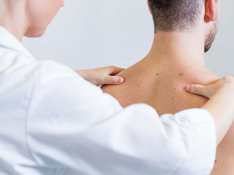 Ärztin untersucht Schultern eines Patienten