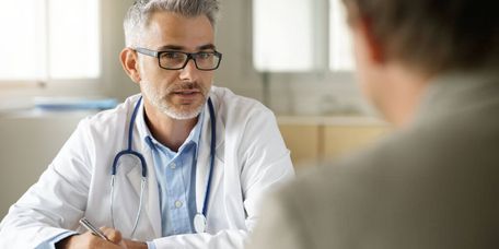 Bärtiger mittelater Arzt spricht mit einem Patienten