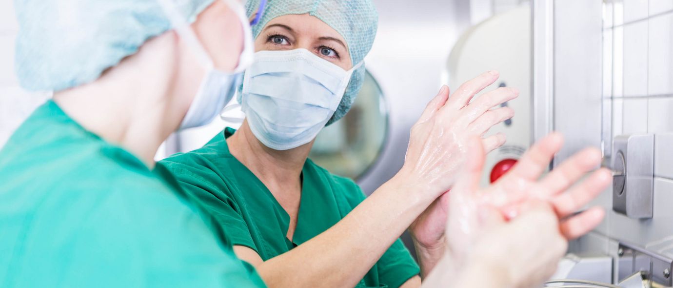 Ärztinnen und Ärzte mit Mundschutz desinfizieren vor einer Operation ihre Hände